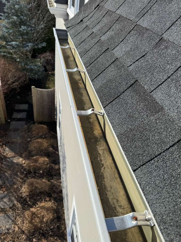 Gutter cleaning service in Massachusetts — close-up of residential roof and aluminum gutter being cleared by Limi Landscaping