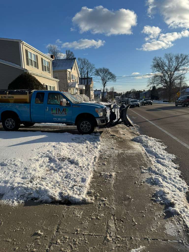 Snow removal service in Massachusetts — Limi Landscaping blue plow truck clearing a residential street after a winter storm